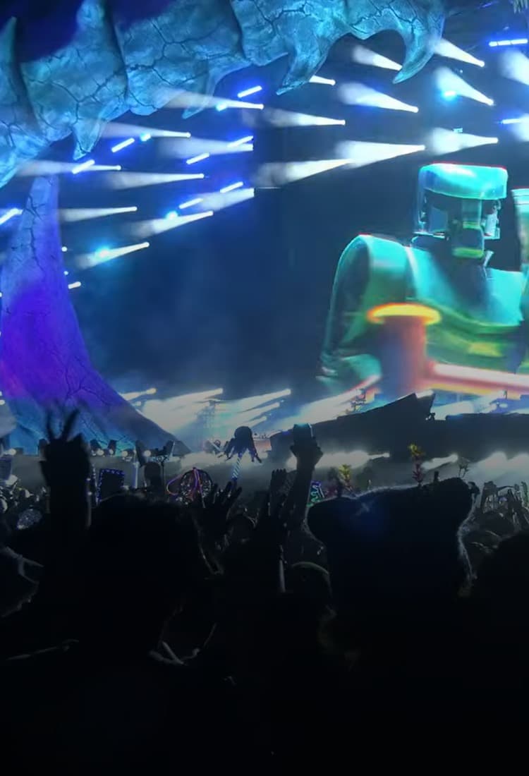Colorful stage lighting illuminates a concert stage above crowd silhouettes.